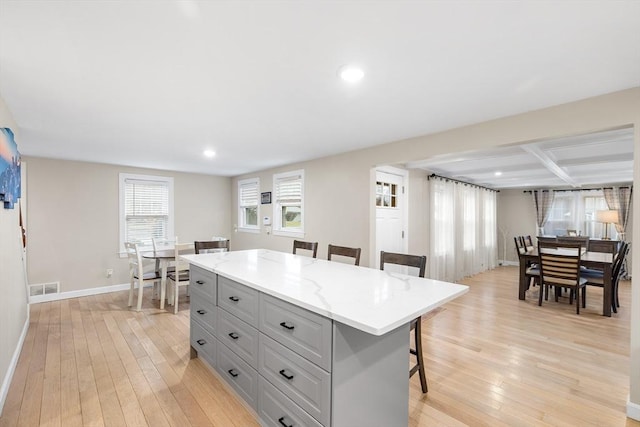 kitchen featuring visible vents, a kitchen island, baseboards, a breakfast bar, and light wood-type flooring