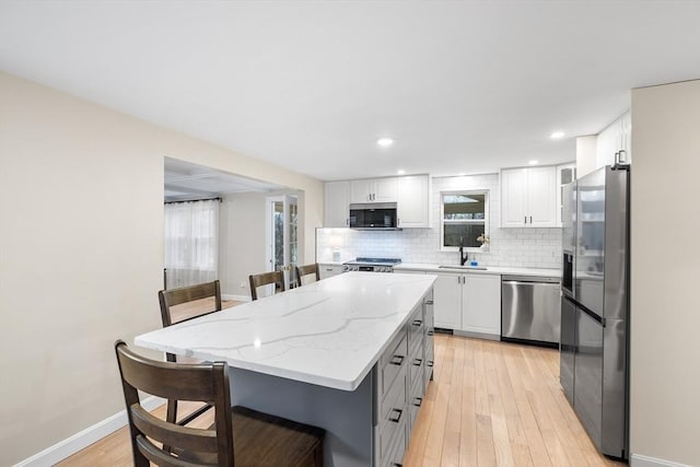 kitchen with a sink, a kitchen breakfast bar, backsplash, stainless steel appliances, and light wood-style floors