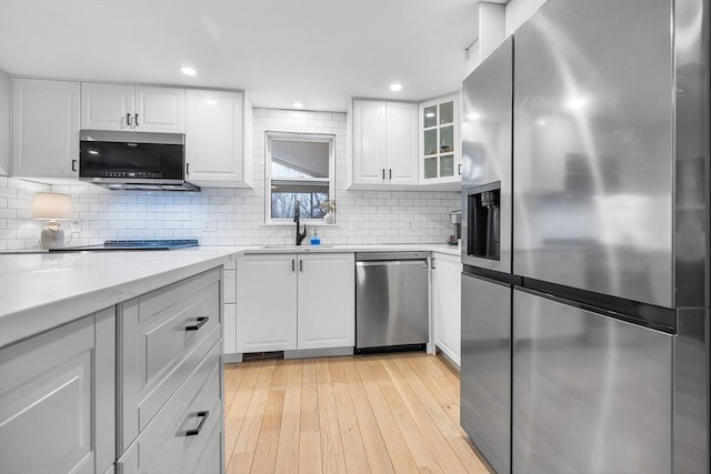 kitchen featuring stainless steel appliances, tasteful backsplash, light wood-style flooring, and white cabinetry