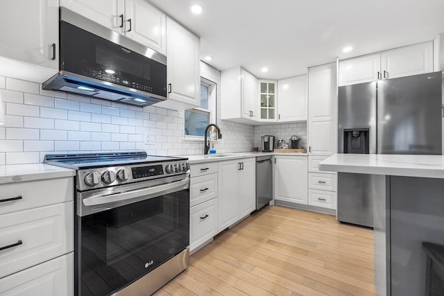 kitchen featuring light wood-style flooring, a sink, backsplash, stainless steel appliances, and white cabinets