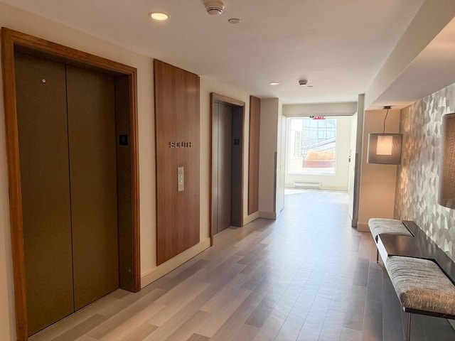 hall featuring elevator, light wood-style flooring, baseboards, and recessed lighting