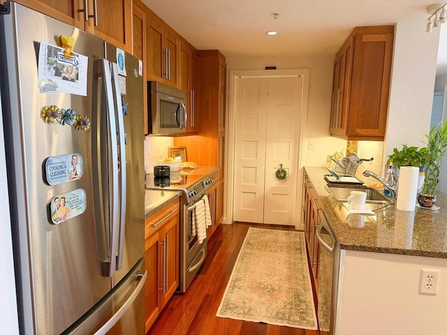 kitchen with stainless steel appliances, dark wood-style flooring, a sink, tasteful backsplash, and brown cabinets