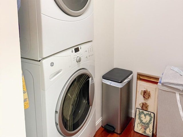 clothes washing area with stacked washer / dryer, wood finished floors, and baseboards