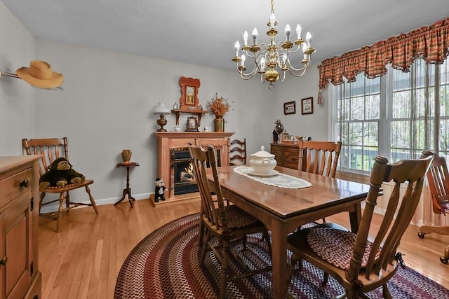 dining room featuring baseboards, light wood finished floors, an inviting chandelier, and a glass covered fireplace