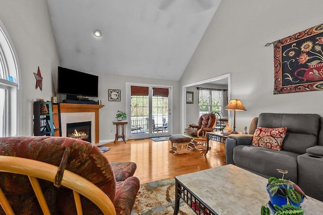 living room with recessed lighting, high vaulted ceiling, a tiled fireplace, and wood finished floors
