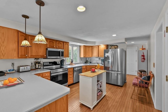 kitchen featuring a sink, stainless steel appliances, pendant lighting, light wood-type flooring, and light countertops