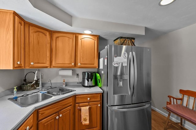 kitchen with brown cabinetry, a sink, stainless steel fridge with ice dispenser, wood finished floors, and light countertops