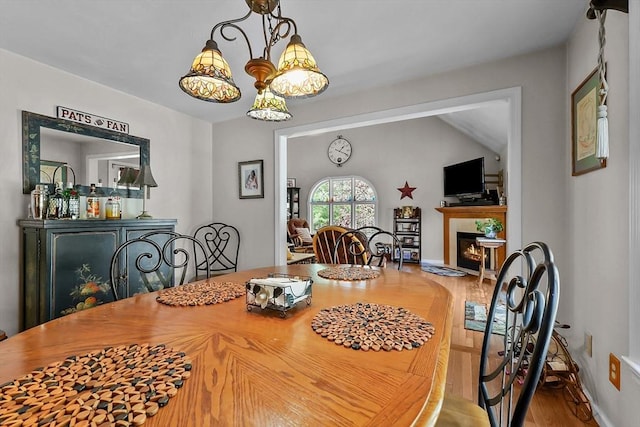 dining room with a notable chandelier, a glass covered fireplace, and wood finished floors