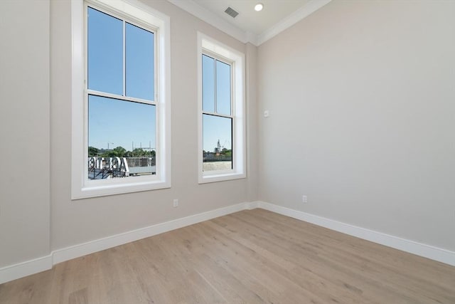 empty room with ornamental molding, light wood-type flooring, visible vents, and baseboards