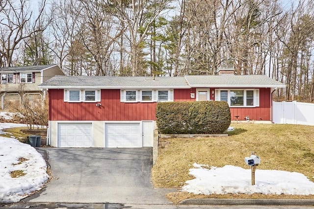 view of front of house featuring aphalt driveway, an attached garage, fence, a front lawn, and a chimney