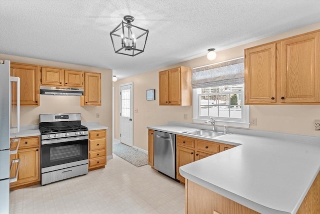 kitchen with sink, appliances with stainless steel finishes, a textured ceiling, light brown cabinetry, and decorative light fixtures