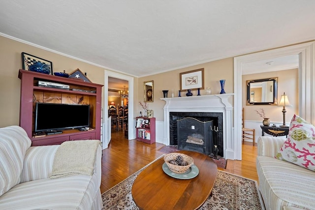 living area with ornamental molding, a fireplace with flush hearth, and wood finished floors