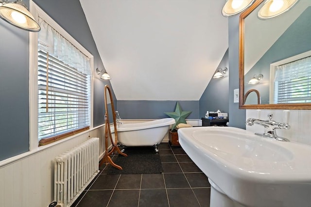 bathroom featuring lofted ceiling, radiator, tile patterned floors, wainscoting, and a freestanding tub
