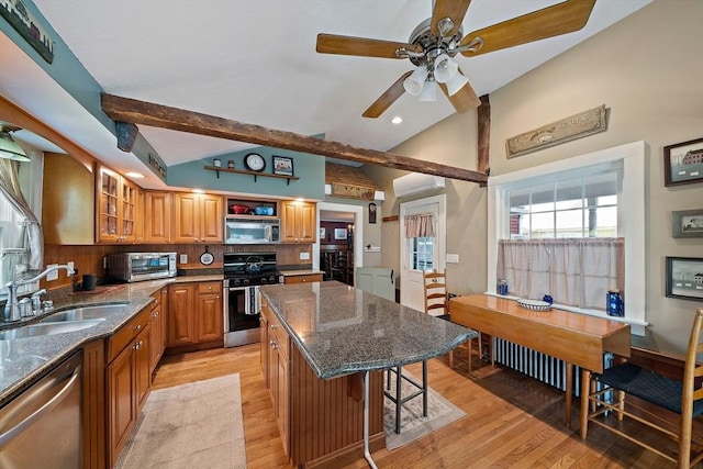 kitchen featuring a sink, stainless steel appliances, dark stone countertops, light wood finished floors, and a ceiling fan