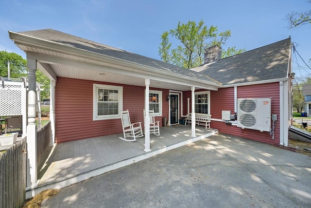 back of property with ac unit, a chimney, a porch, and a shingled roof