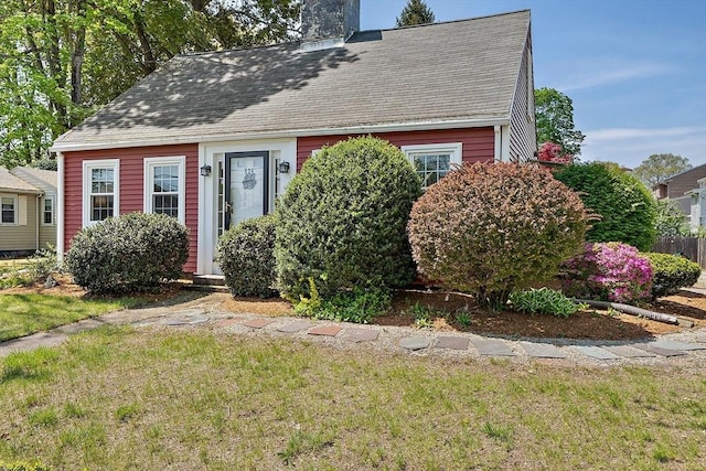cape cod house with roof with shingles, a chimney, and a front yard