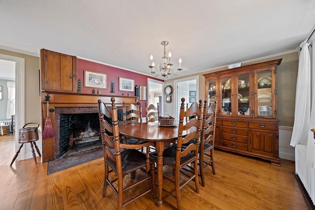 dining area with ornamental molding, a notable chandelier, a fireplace, and light wood-type flooring