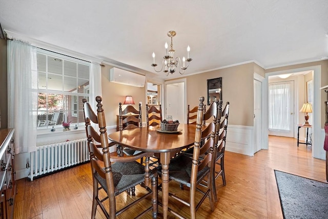 dining room with radiator, a wainscoted wall, light wood-style floors, and a notable chandelier