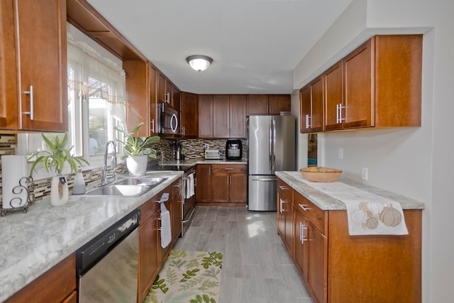 kitchen featuring light stone counters, sink, decorative backsplash, stainless steel appliances, and light hardwood / wood-style flooring