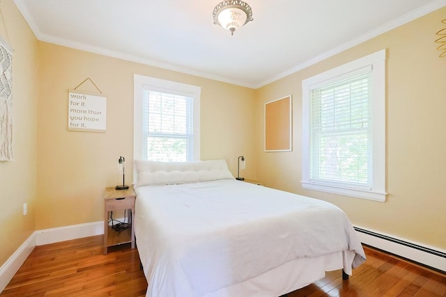 bedroom with crown molding, baseboard heating, and wood finished floors