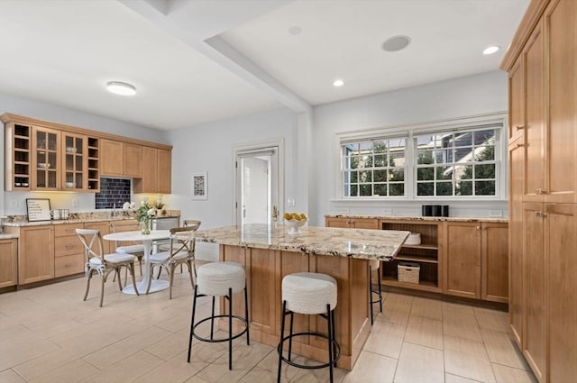 kitchen featuring open shelves, a breakfast bar area, light stone counters, and glass insert cabinets