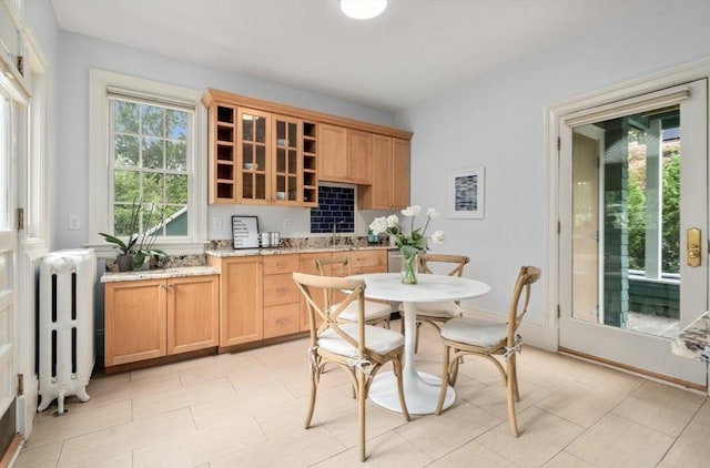 kitchen featuring radiator, glass insert cabinets, light brown cabinetry, light stone counters, and open shelves