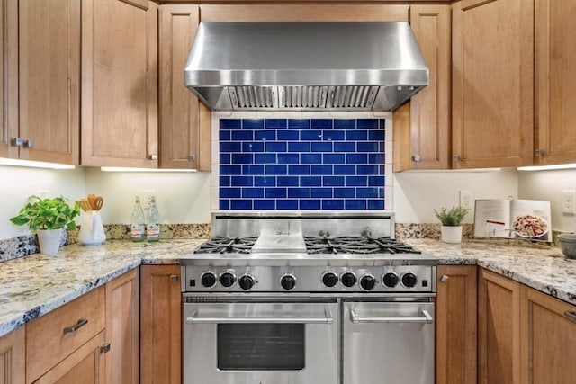 kitchen featuring range with two ovens, light stone counters, tasteful backsplash, and wall chimney range hood