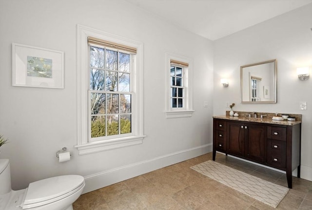 bathroom featuring vanity, toilet, a healthy amount of sunlight, and baseboards