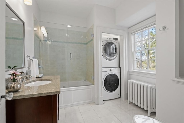 full bath featuring tile patterned floors, radiator heating unit, stacked washing maching and dryer, enclosed tub / shower combo, and vanity