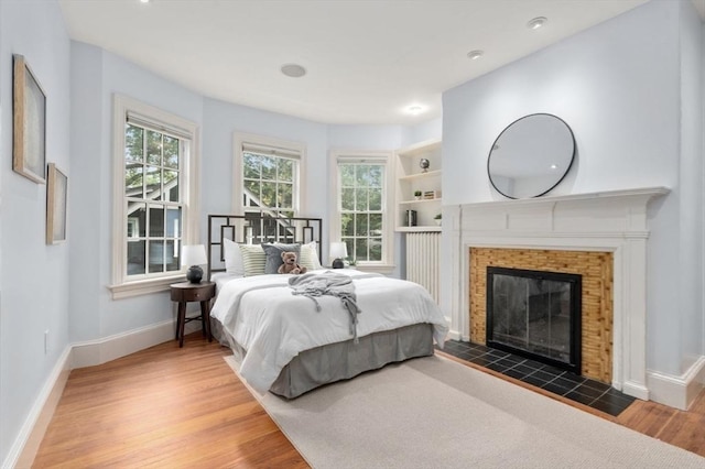 bedroom featuring multiple windows, a fireplace, baseboards, and wood finished floors