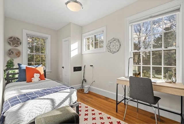 bedroom with multiple windows, wood finished floors, and baseboards