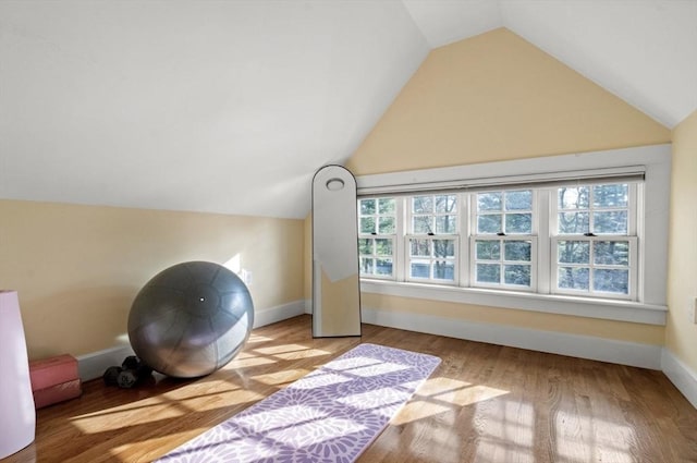 exercise area featuring baseboards, plenty of natural light, wood finished floors, and vaulted ceiling