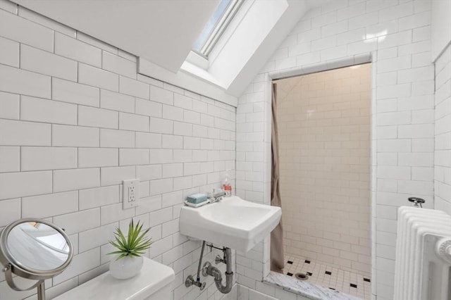 full bath featuring lofted ceiling with skylight, a stall shower, a sink, radiator heating unit, and tile walls