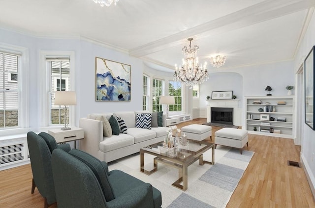 living area featuring crown molding, light wood-style flooring, a notable chandelier, and a fireplace