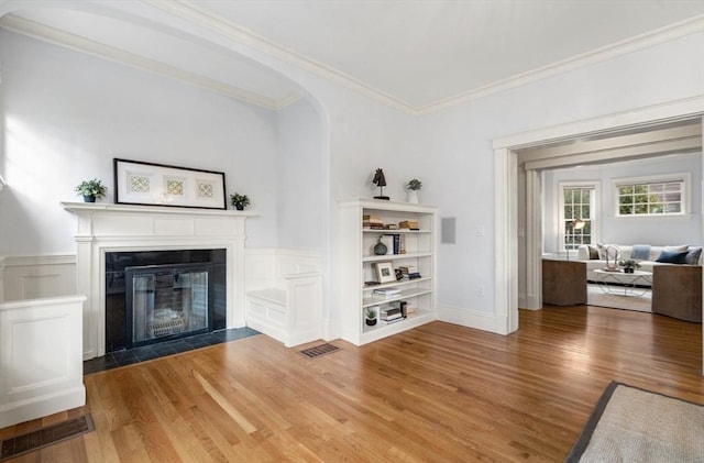 unfurnished living room featuring visible vents, a fireplace with flush hearth, wood finished floors, and ornamental molding