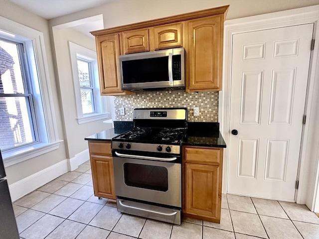 kitchen featuring light tile patterned flooring, stainless steel appliances, decorative backsplash, and dark stone counters