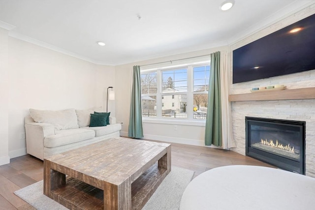 living room with crown molding, a stone fireplace, and light hardwood / wood-style flooring