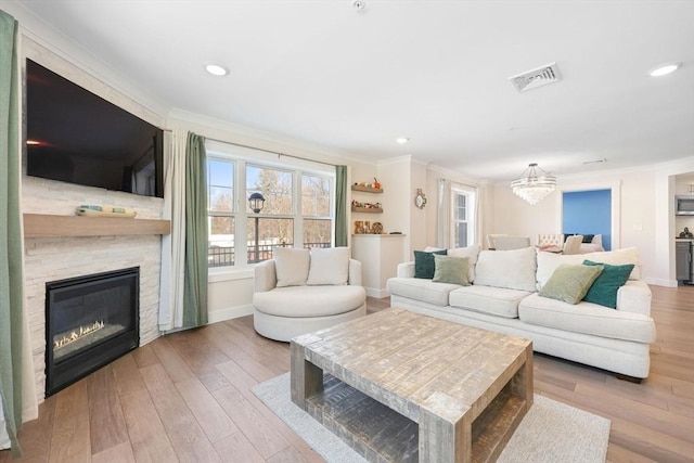 living room featuring crown molding, a fireplace, light hardwood / wood-style floors, and a chandelier