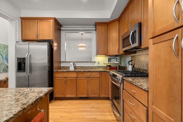 kitchen with stone countertops, hanging light fixtures, light wood-type flooring, and appliances with stainless steel finishes