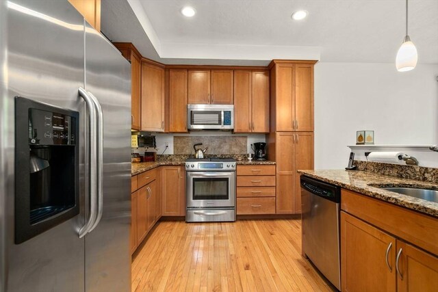 kitchen with decorative light fixtures, appliances with stainless steel finishes, light hardwood / wood-style floors, sink, and dark stone counters