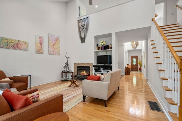 living room featuring light wood-type flooring, a tile fireplace, and a high ceiling