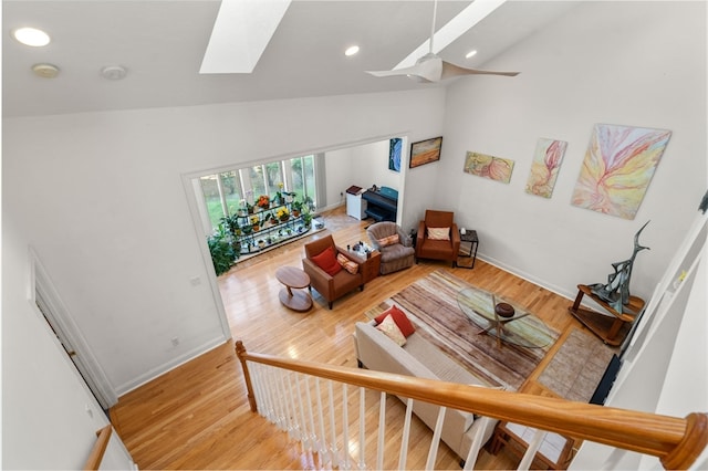 living room with high vaulted ceiling, a skylight, and light hardwood / wood-style floors