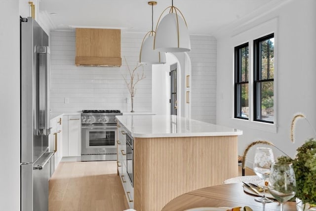 kitchen with pendant lighting, a center island, high end appliances, ornamental molding, and white cabinetry