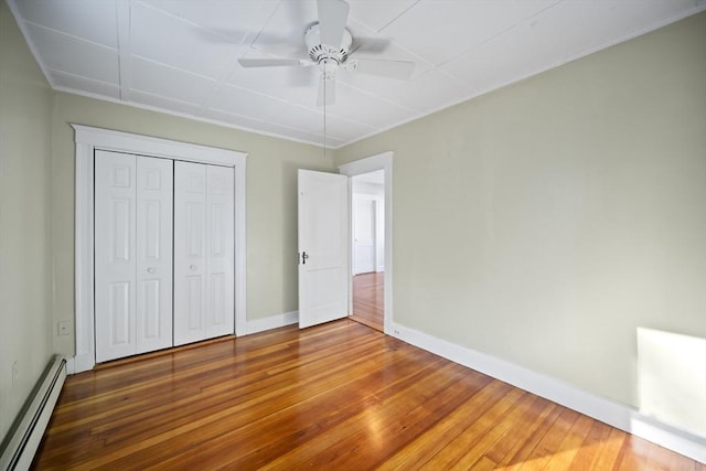 unfurnished bedroom with hardwood / wood-style flooring, ceiling fan, a closet, and a baseboard heating unit