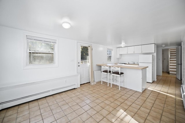 kitchen with kitchen peninsula, a kitchen breakfast bar, baseboard heating, white fridge, and white cabinetry