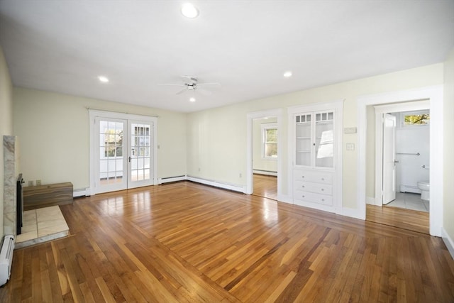 unfurnished living room featuring wood-type flooring, baseboard heating, a wealth of natural light, and ceiling fan