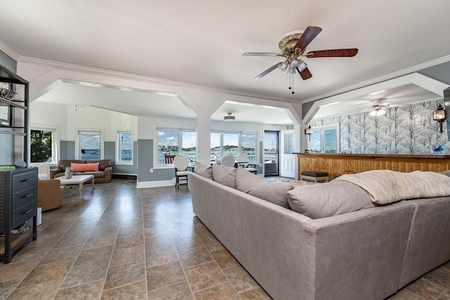 living room featuring a ceiling fan, baseboards, stone finish floors, and crown molding
