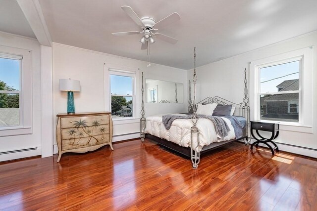 bedroom with a baseboard heating unit, multiple windows, wood finished floors, ornamental molding, and a ceiling fan