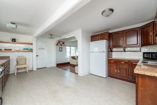 kitchen with freestanding refrigerator, arched walkways, black microwave, decorative backsplash, and baseboards