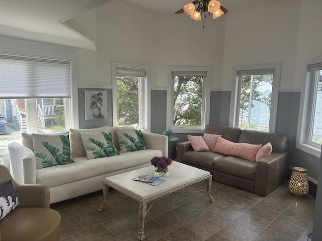 living area with a ceiling fan, a towering ceiling, and dark stone finish floors
